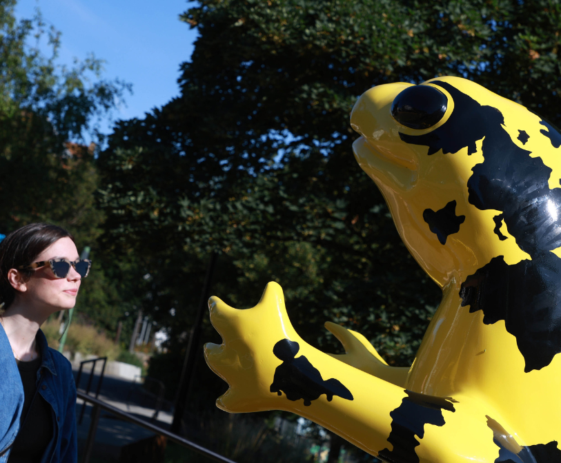 A photograph of a woman looking at Monster Chetwynd’s giant brightly-coloured salamander at Payers Park