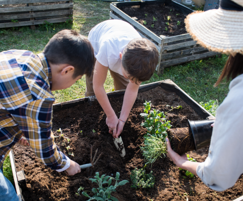 Two young people and an adult making holes for planting in a raised bed.