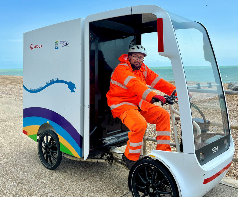 An image of a Veolia crew member using the ebike collection vehicle along Sandgate Beach