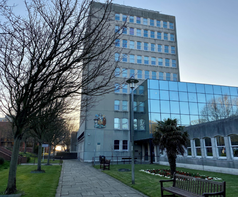 An image of Folkestone Civic Centre in late winter surrounded by green grass and bare trees as well as a row of benches