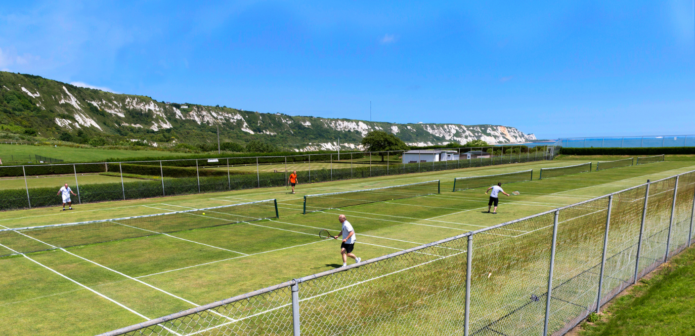 Two games of tennis being played at East Cliff Sports with The Warren in the background.