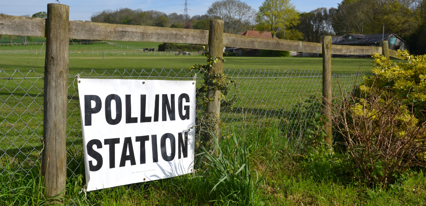 A polling station sign on a fence in the countryside.