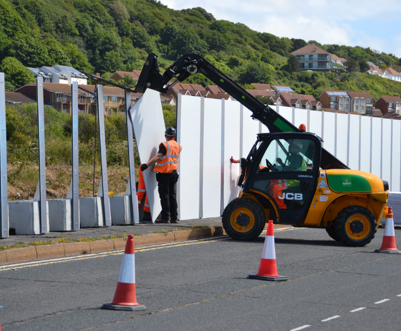 A photograph of two people using machinery to install hoardings at Princes Parade in the summer of 2022
