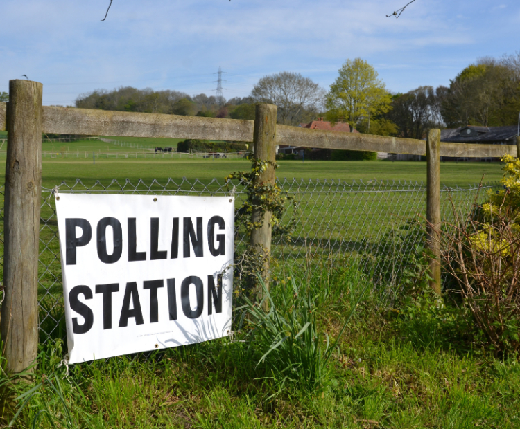 An image of a polling station sign against a fence and field