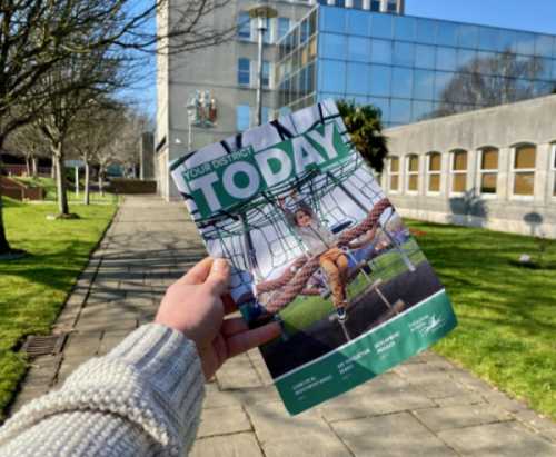 A photograph of an arm and hand holding the Spring 2023 edition of Your District Today.