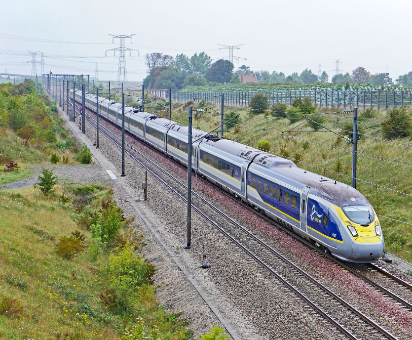 A Eurostar train in motion on tracks surrounded by green space