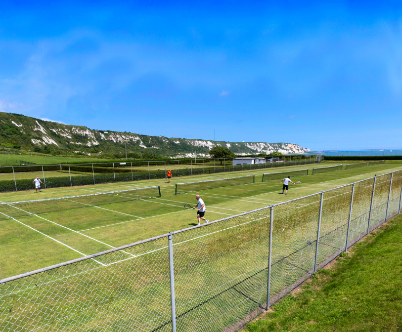 Two games of tennis being played at East Cliff Sports with The Warren in the background.