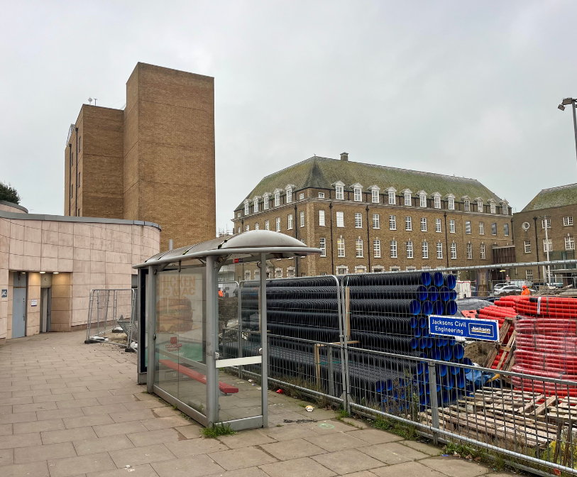A photograph of work taking place at Bouverie Square, with a former bus stop in the foreground and the public toilets visible to the left.