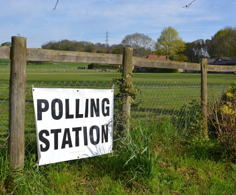 A polling station sign on a fence in the countryside.