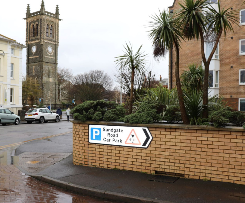 A photograph of a sign pointing towards Sandgate Road car park, with the Christ Church Tower in the background.